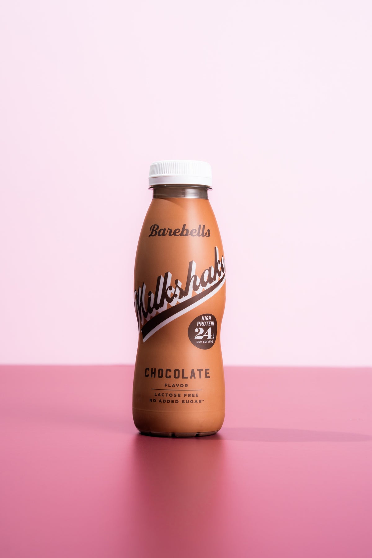 Barebells Milkshake Chocolate flavour bottle with white cap on a pink surface against pink background